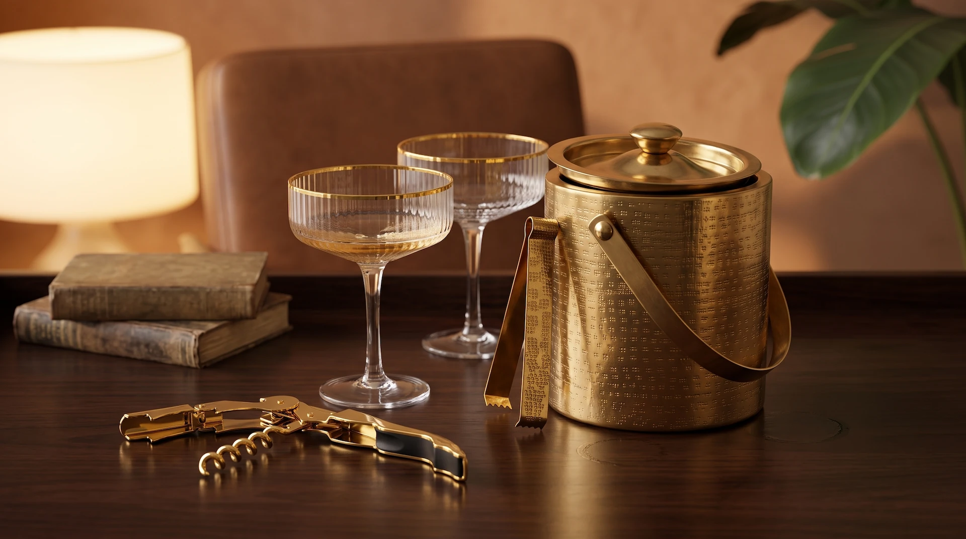 Gold corkscrew, crystal coupe glasses, and a brass ice bucket with tongs styled on a dark lacquered surface
